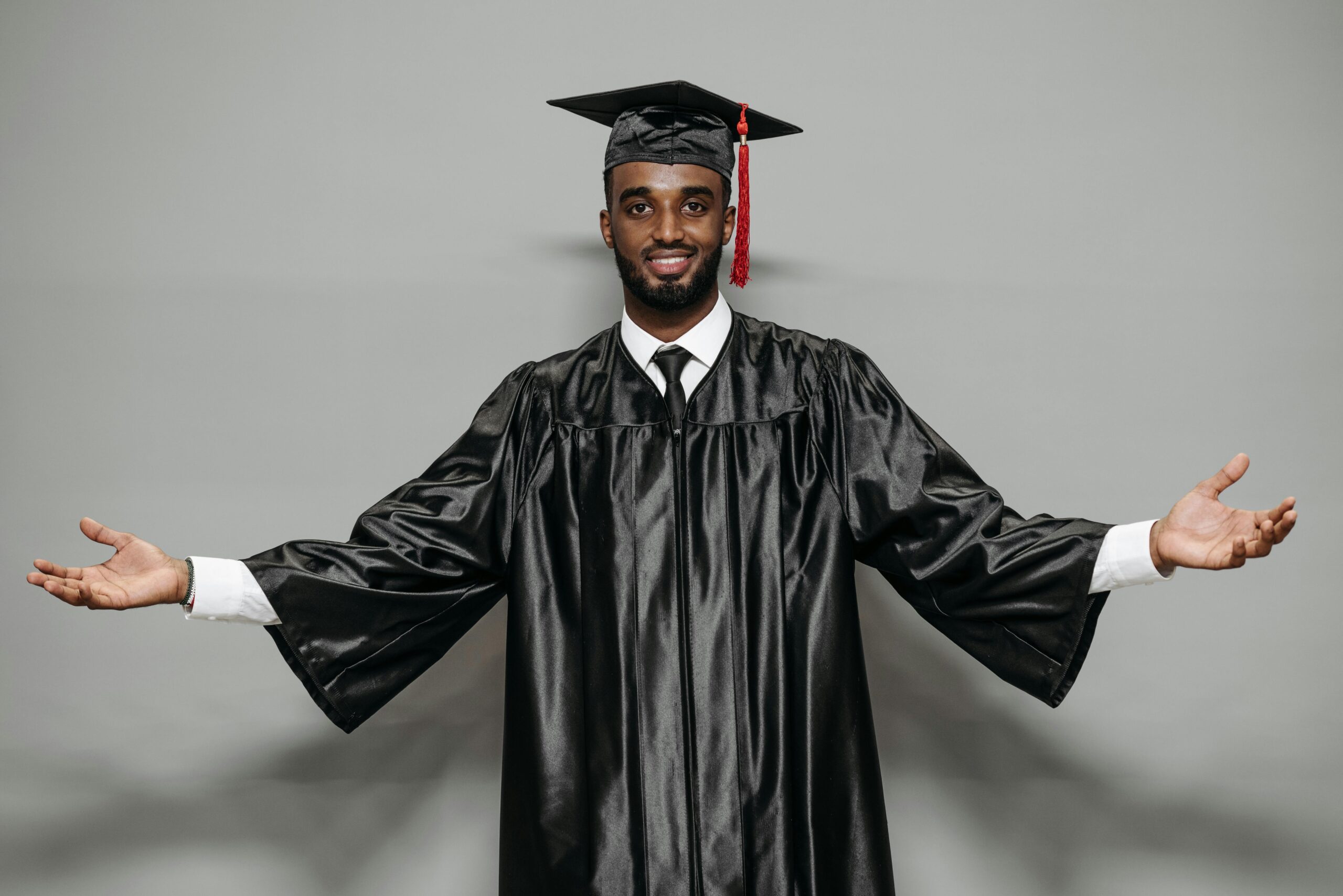 Smiling man in graduation gown celebrating achievement with outstretched arms.